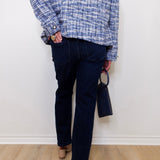 Person wearing a blue plaid shirt and dark jeans against a white wall.
