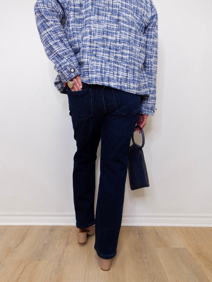 Person wearing a blue plaid shirt and dark jeans against a white wall.