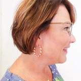 Woman with short brown hair wearing glasses and hoop earrings, smiling.