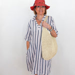 Woman wearing a striped dress and red hat with a straw bag against a white background