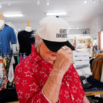 Person wearing a white cap with 'God's Favorite' text in a store setting