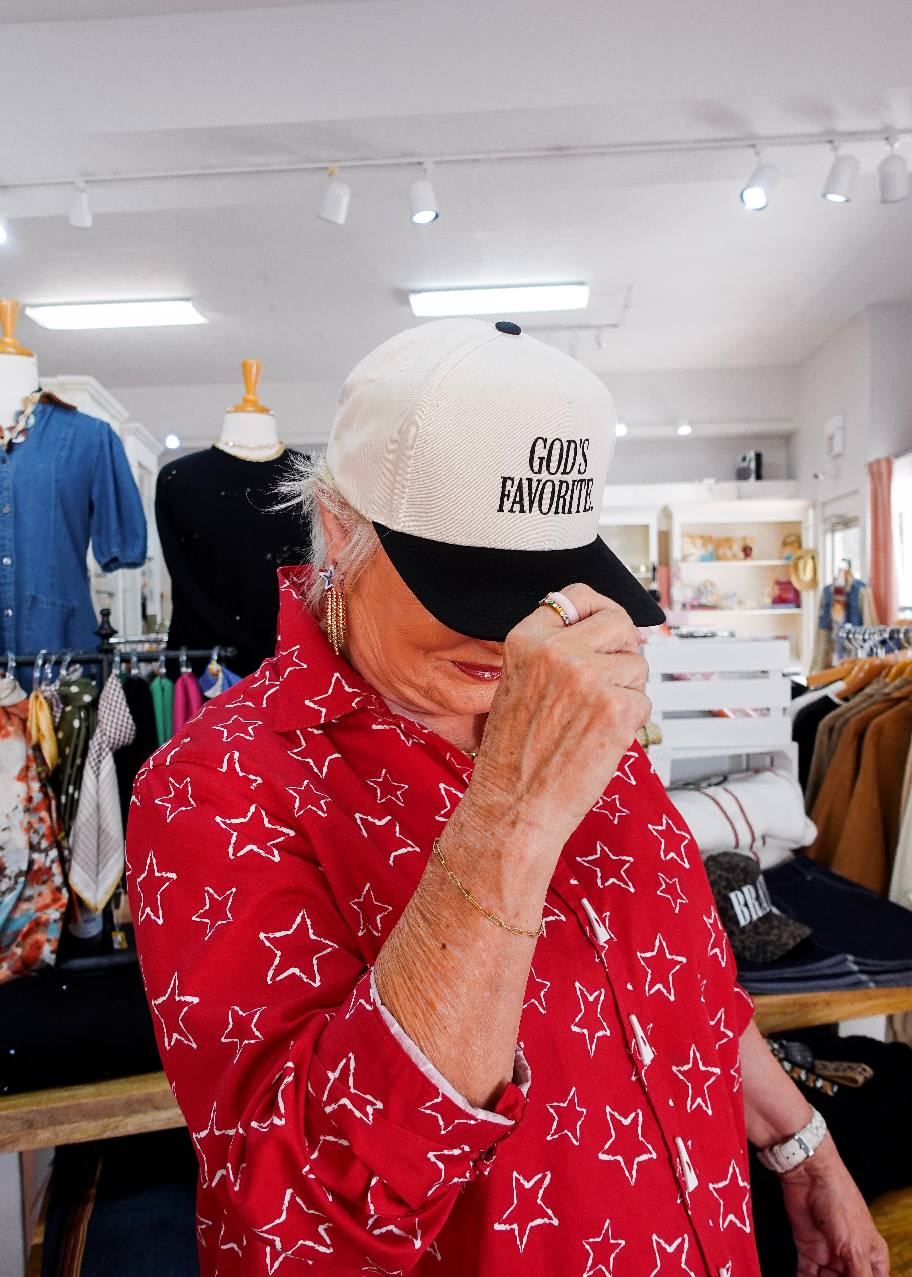 Person wearing a white cap with 'God's Favorite' text in a store setting