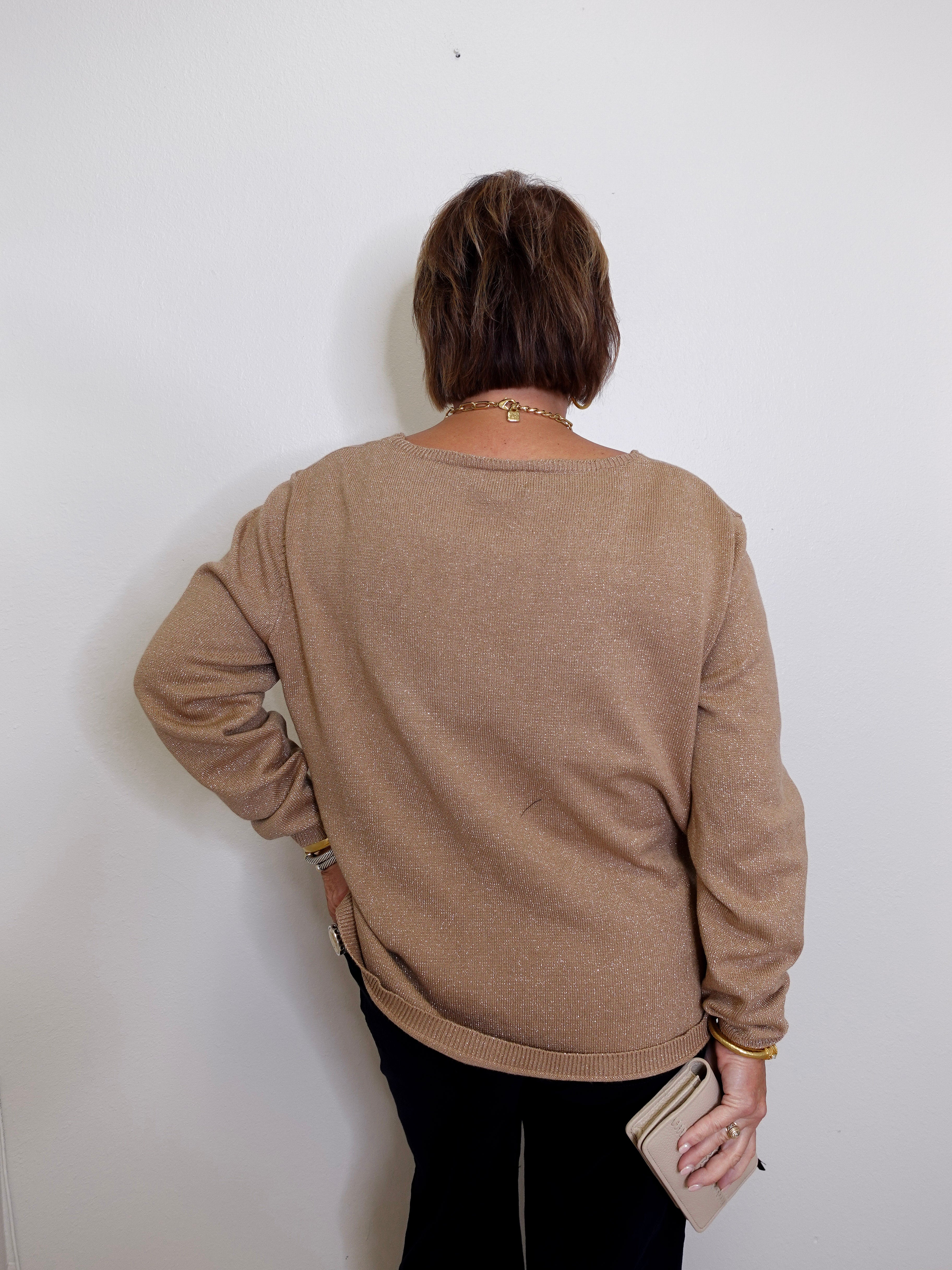 Person wearing a beige sweater against a white wall