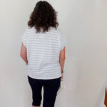 Person wearing a striped shirt and dark shorts standing against a white wall.