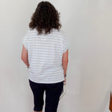 Person wearing a striped shirt and dark shorts standing against a white wall.