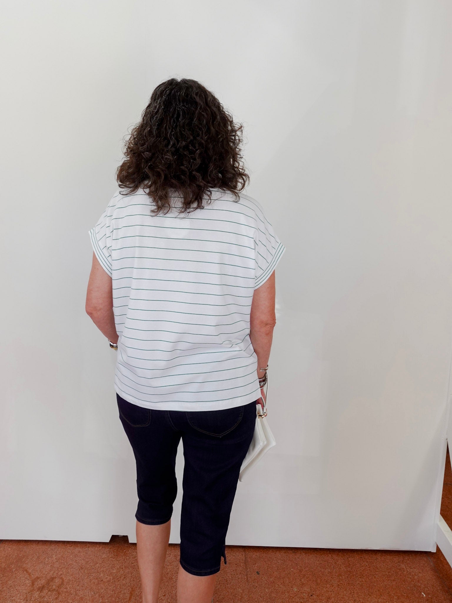 Person wearing a striped shirt and dark shorts standing against a white wall.