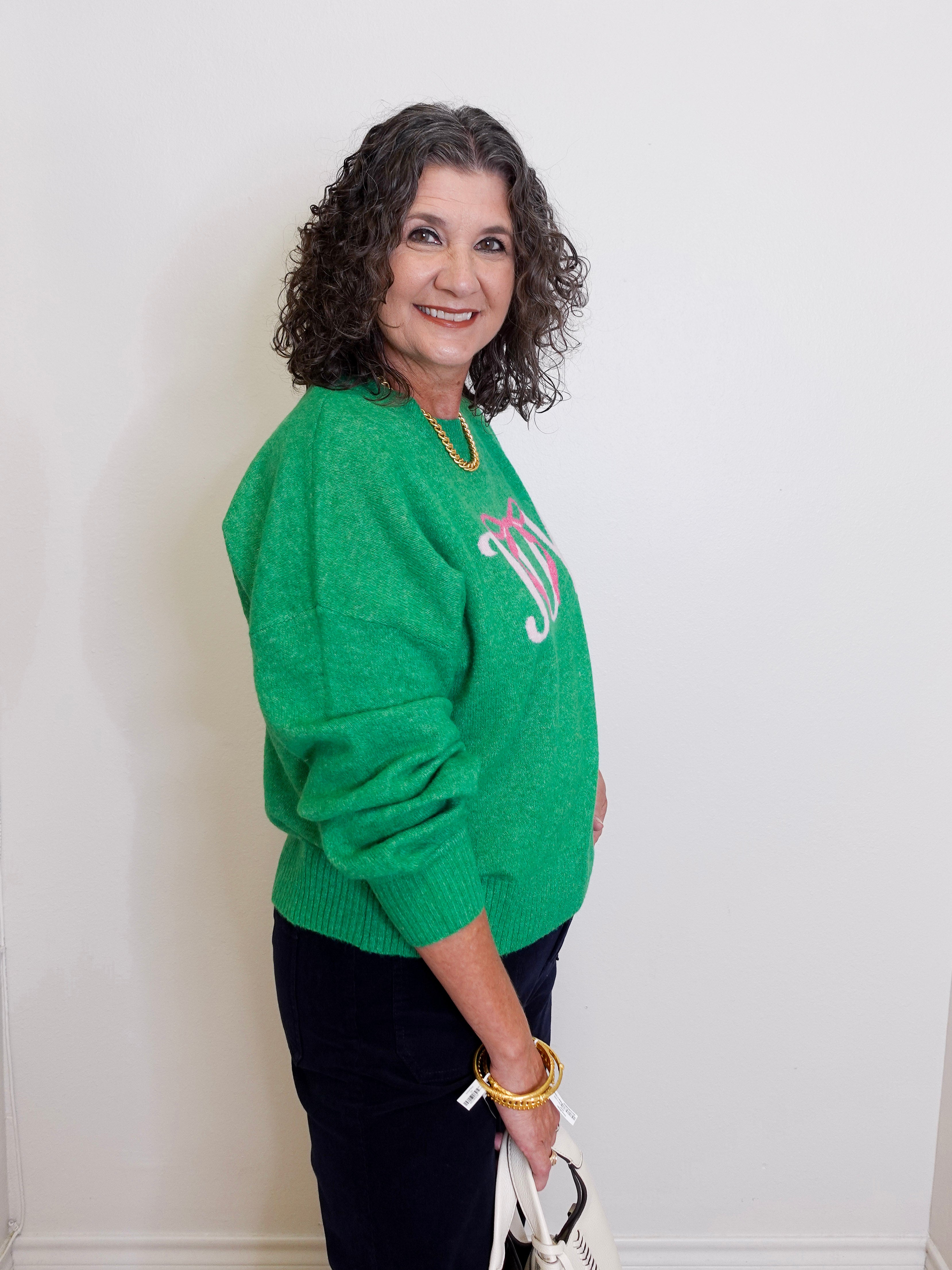 Woman wearing a green sweater with a logo, standing against a white wall.