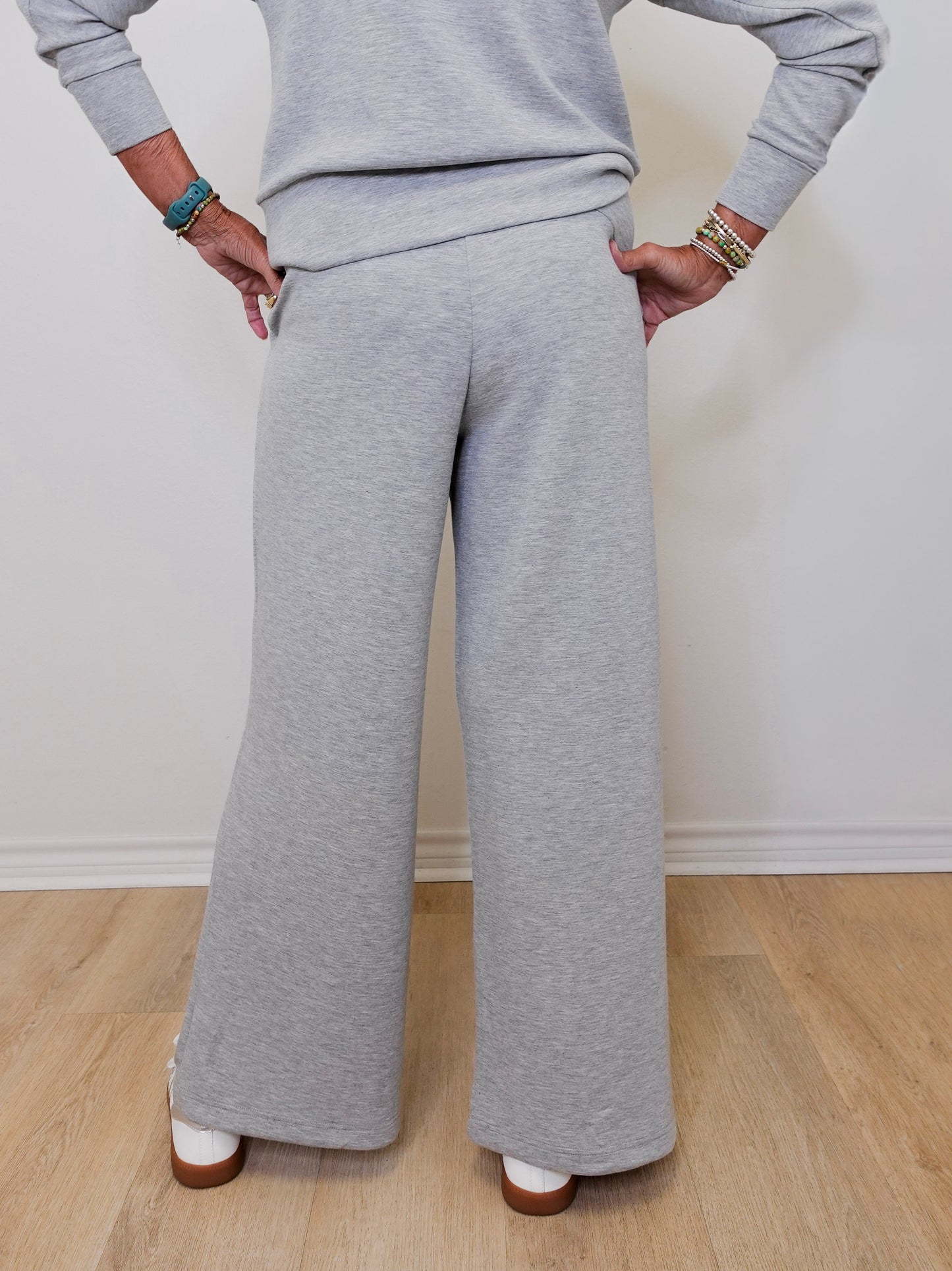 Person wearing a gray outfit with wide-leg pants against a white wall.