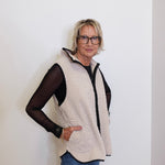 Woman wearing a beige fleece vest over a black top against a white background