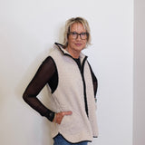 Woman wearing a beige fleece vest over a black top against a white background