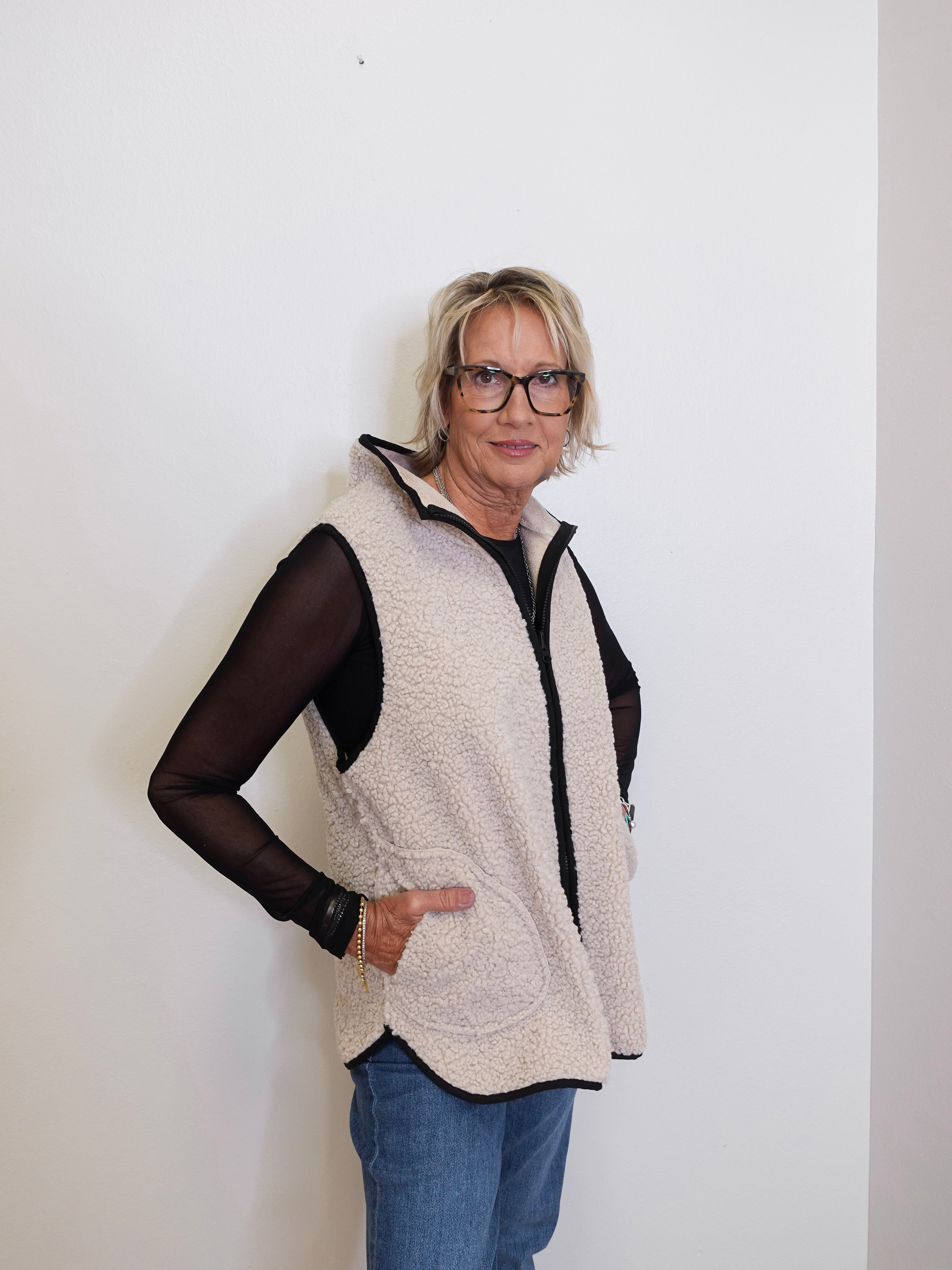 Woman wearing a beige fleece vest over a black top against a white background