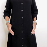 Person wearing a black button-up dress against a white background