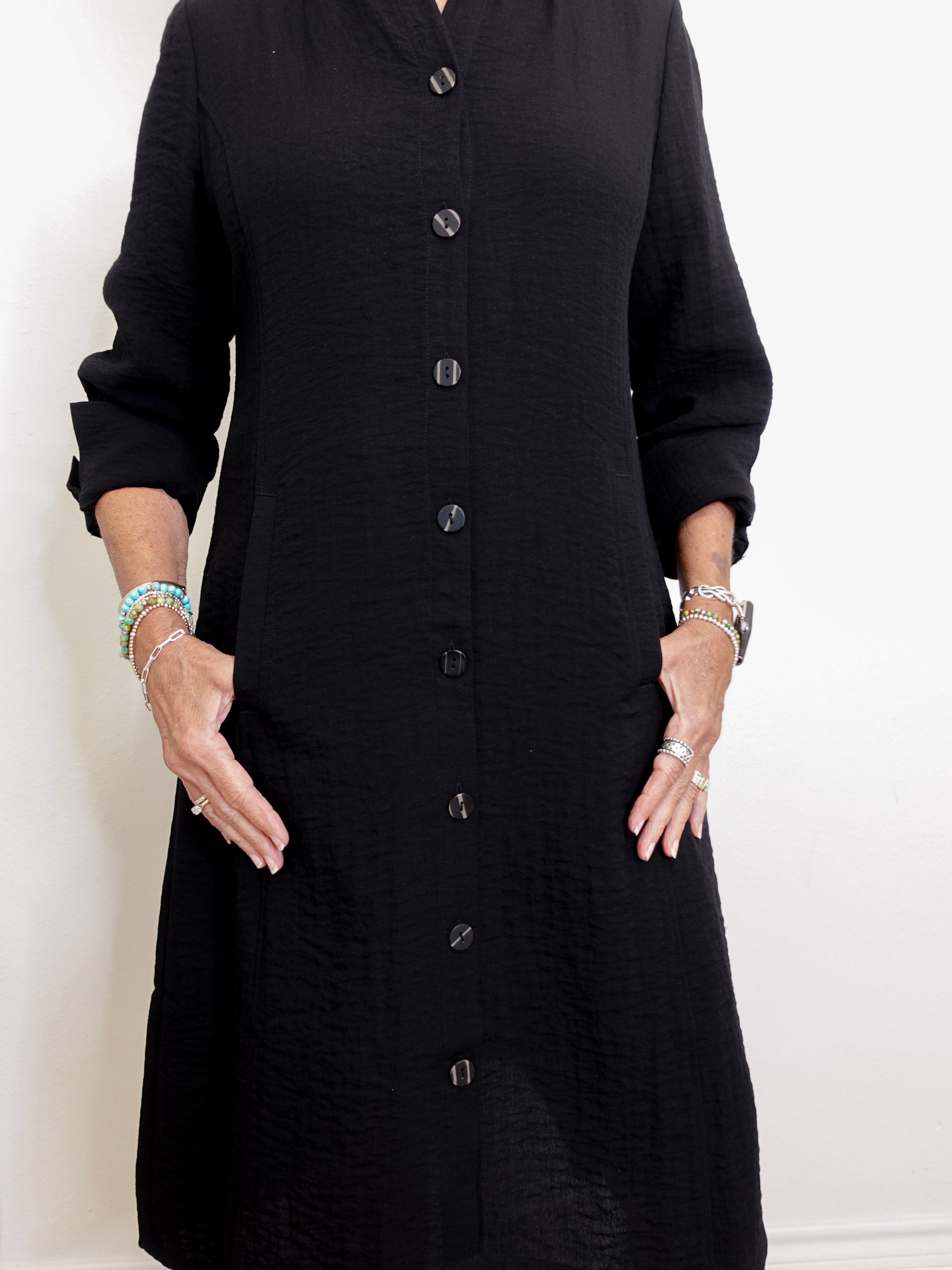 Person wearing a black button-up dress against a white background