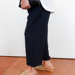 Person wearing black pants and beige sandals on a red tiled floor.