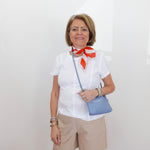 Woman wearing a white blouse with a red scarf, beige shorts, and holding a blue bag against a white background