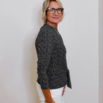 Woman wearing a black patterned blouse and white pants against a plain background