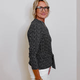 Woman wearing a black patterned blouse and white pants against a plain background