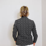 Person wearing a black and white patterned jacket against a plain background