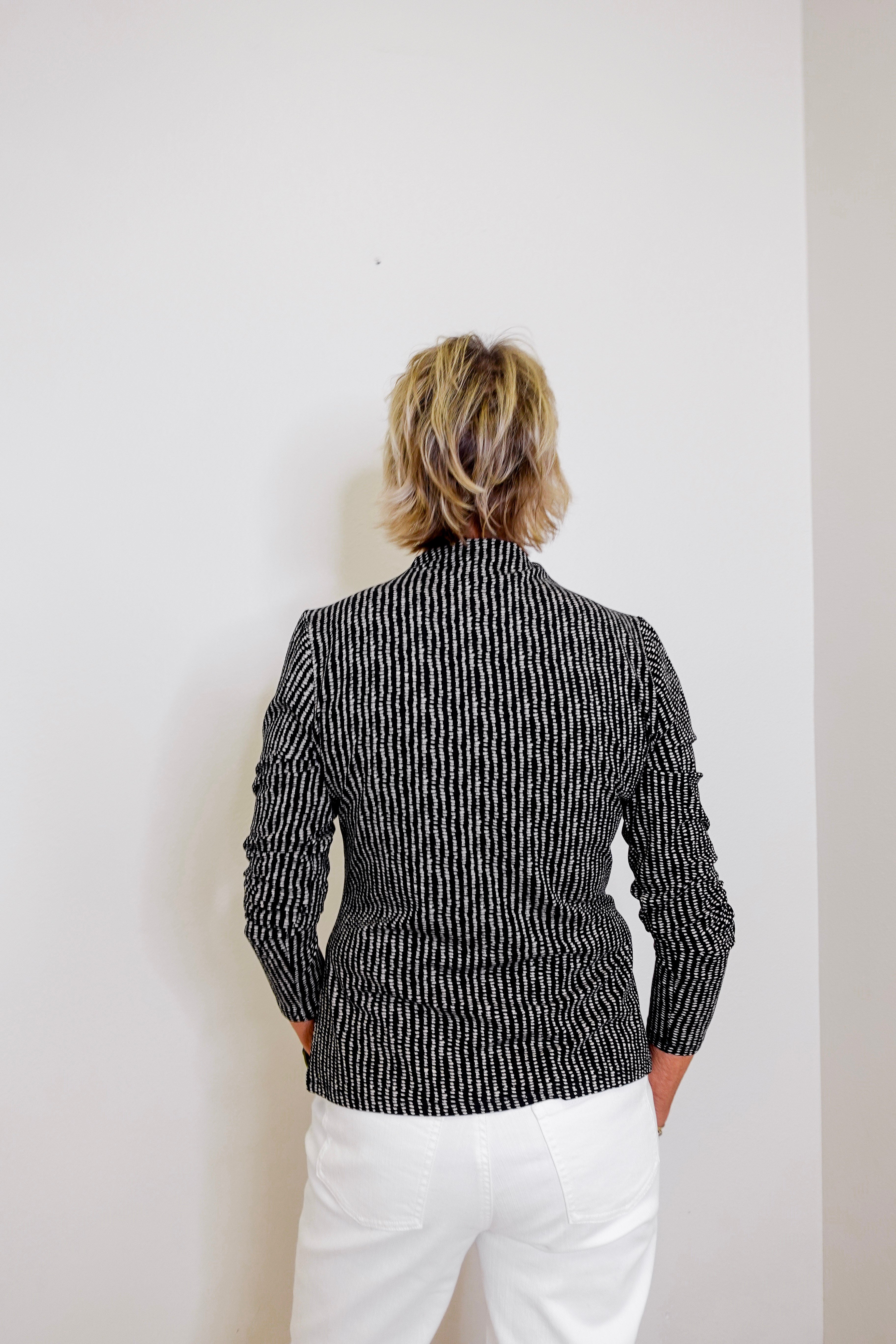 Person wearing a black and white patterned jacket against a plain background