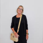 Woman wearing a black outfit with a beige handbag against a white background