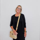 Woman wearing a black outfit with a beige handbag against a white background