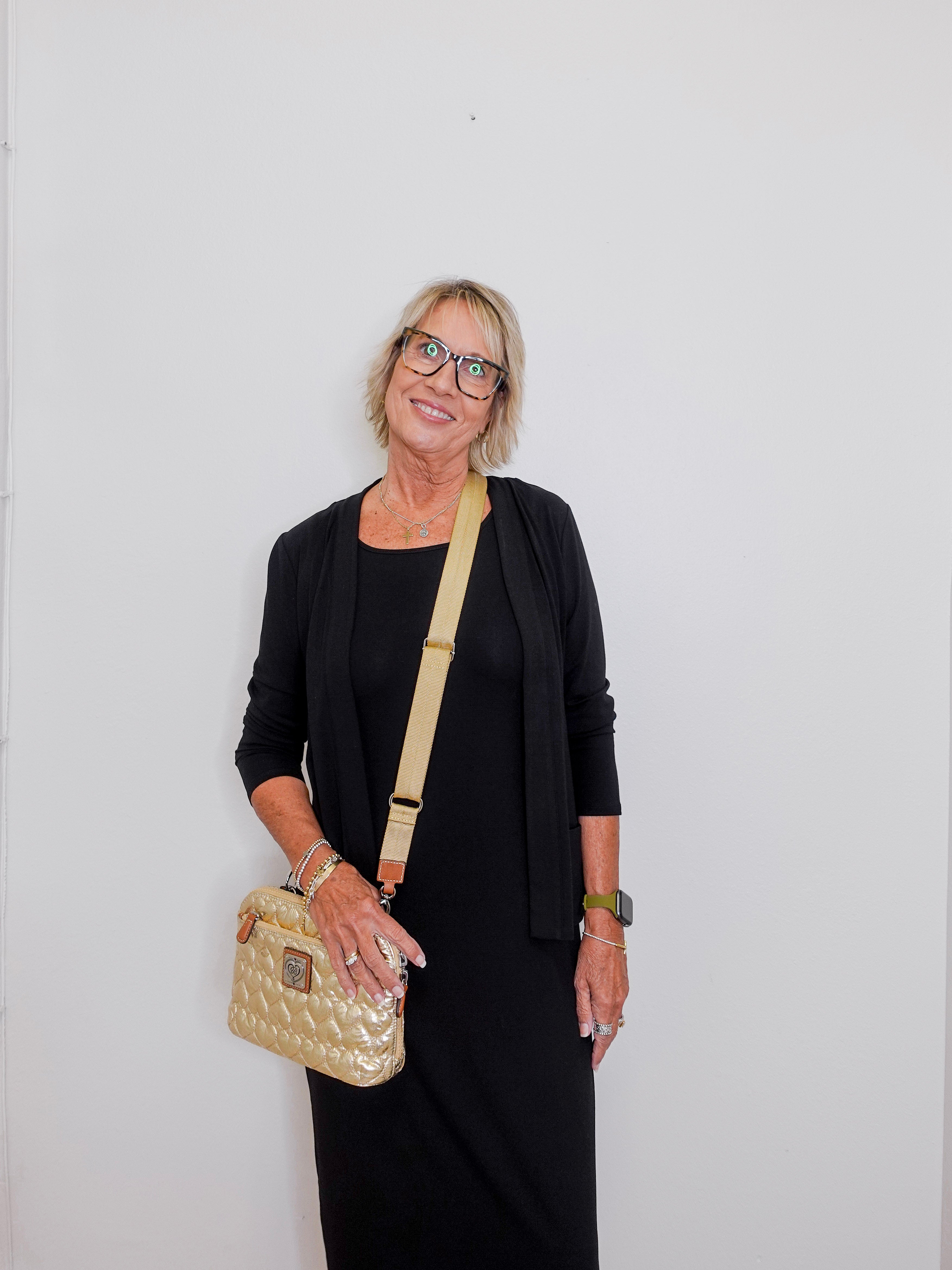 Woman wearing a black outfit with a beige handbag against a white background
