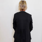 Person wearing a black blazer against a white wall