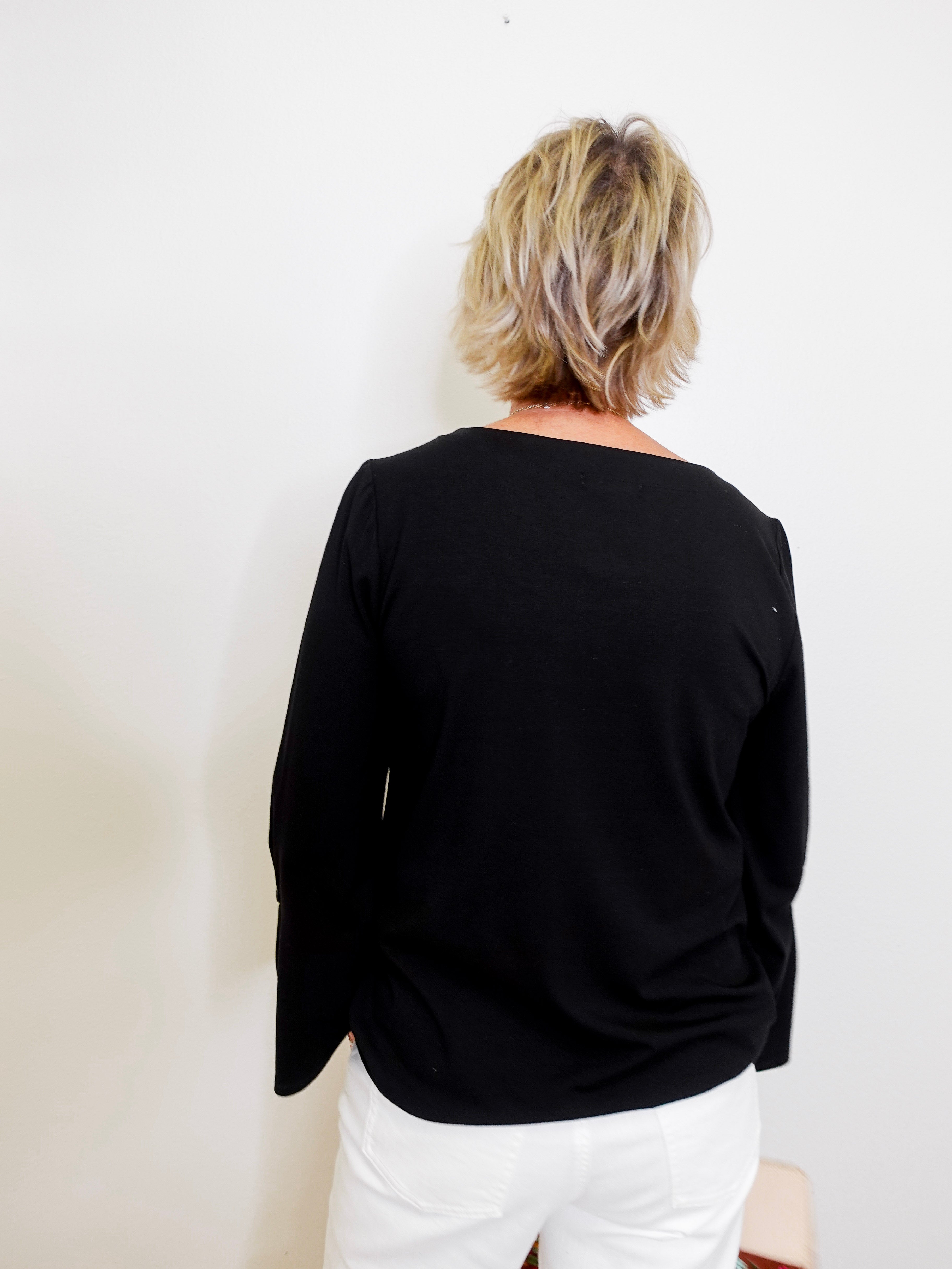 Person wearing a black top and white pants against a plain background