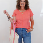 Woman in a coral shirt and blue jeans holding a colorful scarf against a white background
