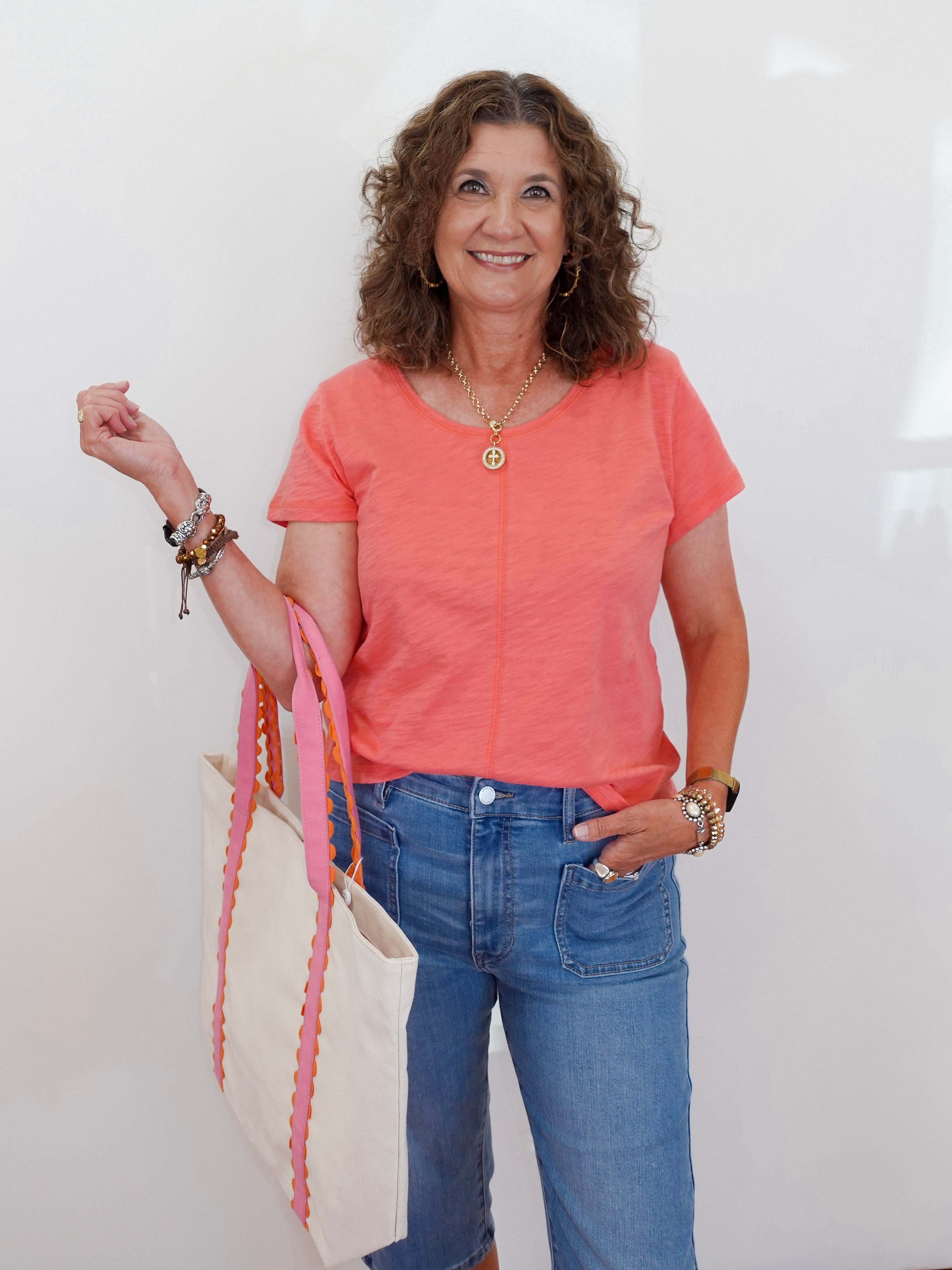 Woman in a coral shirt and blue jeans holding a colorful scarf against a white background