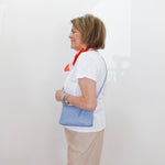 Woman wearing a white shirt with blue accents and beige skirt against a white wall.