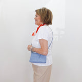Woman wearing a white shirt with blue accents and beige skirt against a white wall.