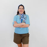 Woman wearing a blue shirt, green shorts, and a colorful scarf with arms crossed against a white background