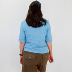 Person wearing a blue shirt and brown shorts against a white wall