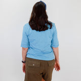 Person wearing a blue shirt and brown shorts against a white wall