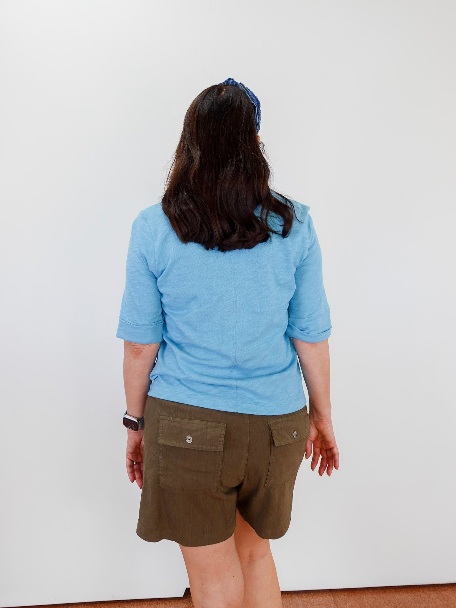 Person wearing a blue shirt and brown shorts against a white wall
