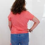 Person wearing a pink shirt and blue jeans standing against a white wall.