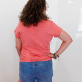 Person wearing a pink shirt and blue jeans standing against a white wall.