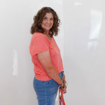 Woman wearing a pink shirt and blue jeans holding a bag against a white background