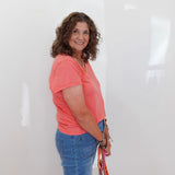 Woman wearing a pink shirt and blue jeans holding a bag against a white background
