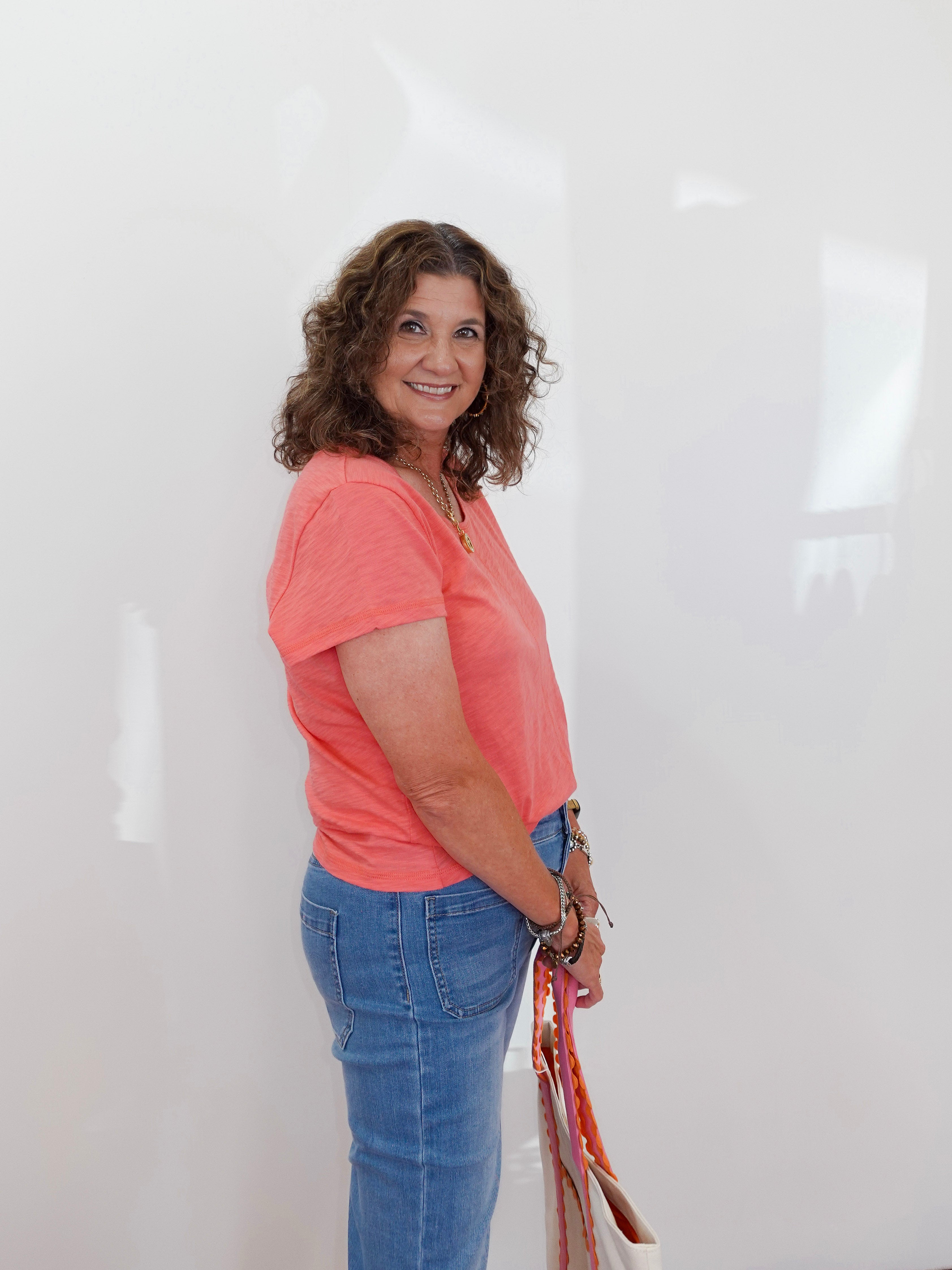 Woman wearing a pink shirt and blue jeans holding a bag against a white background