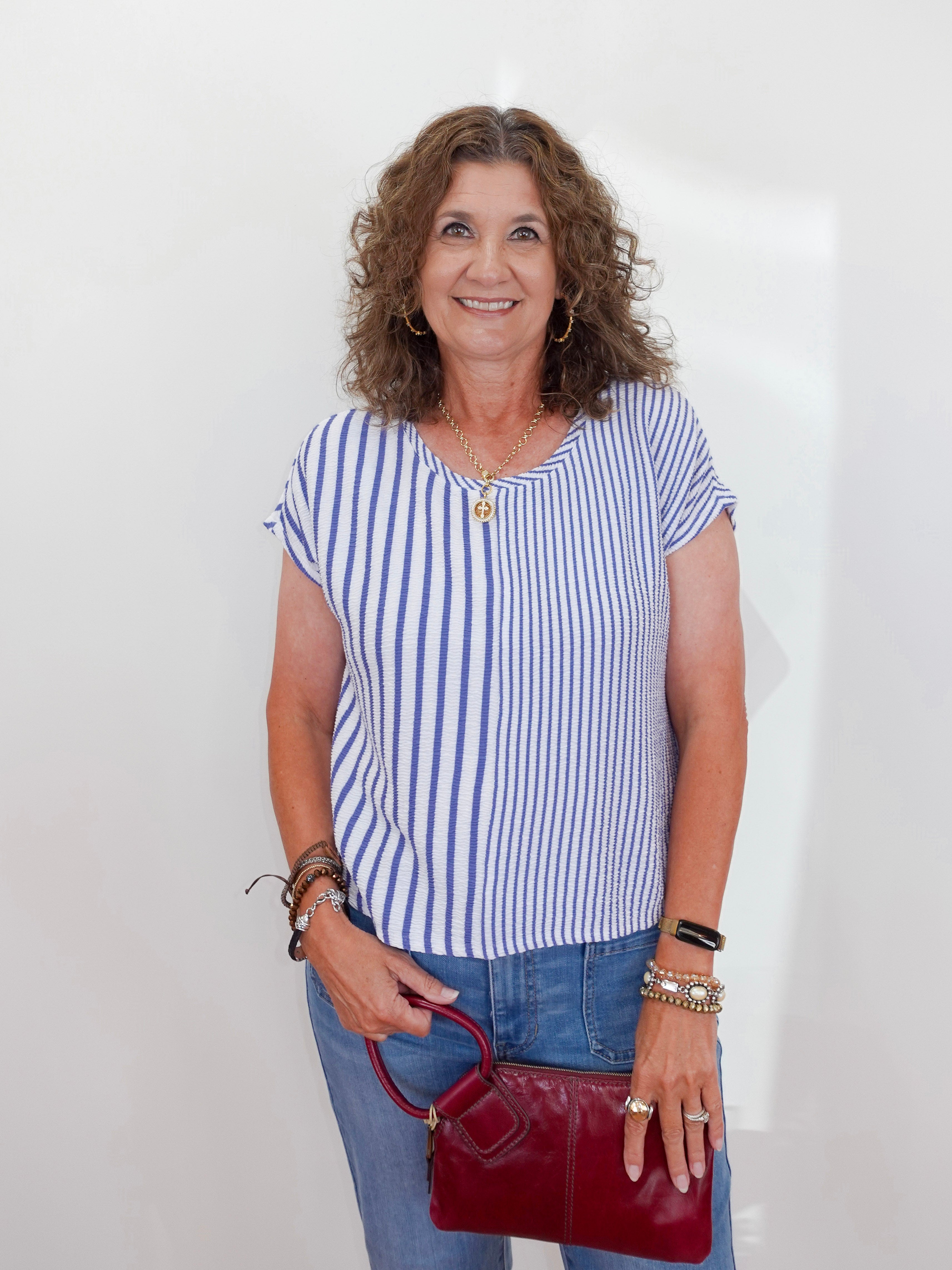 Woman wearing a blue and white striped shirt and jeans, holding a red handbag against a white background