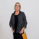 Woman wearing a black polka dot jacket over a black top, holding a yellow bag against a white background