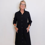 Woman wearing a black dress standing against a white wall