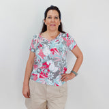 Woman wearing a colorful floral shirt and beige shorts against a white background