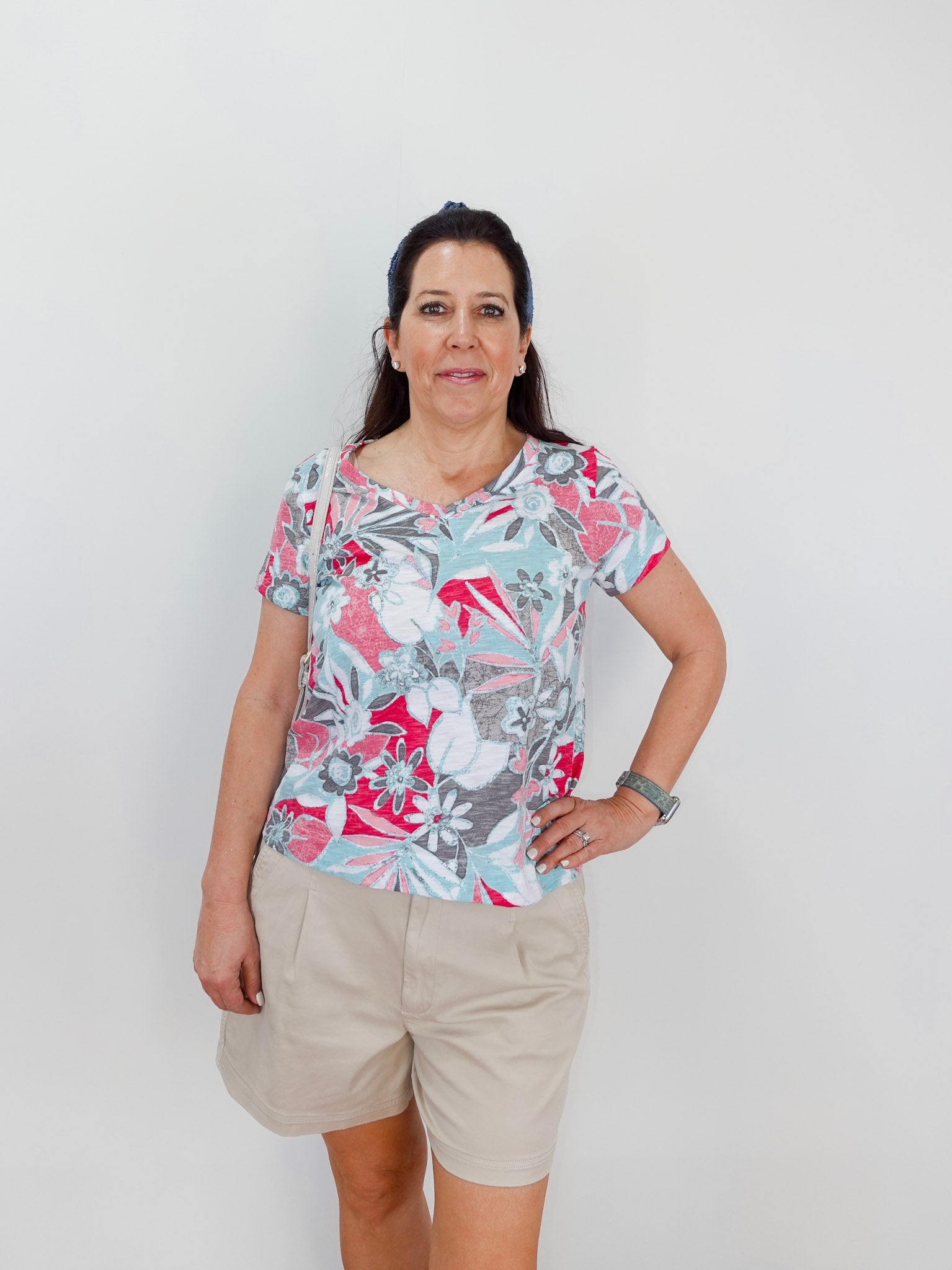 Woman wearing a colorful floral shirt and beige shorts against a white background