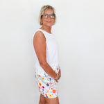 Woman wearing a white sleeveless top and colorful floral shorts against a plain background