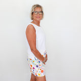Woman wearing a white sleeveless top and colorful floral shorts against a plain background