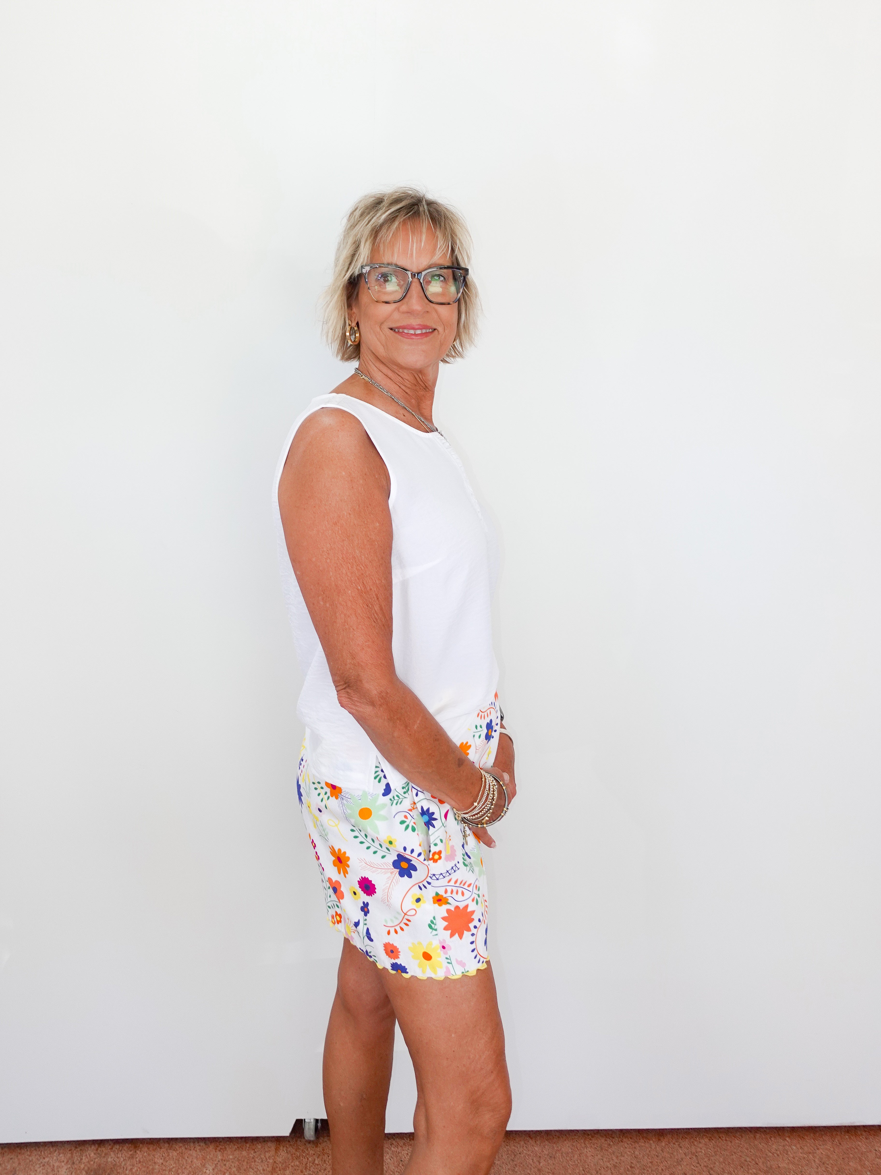 Woman wearing a white sleeveless top and colorful floral shorts against a plain background