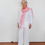 Woman wearing a pink scarf and white outfit against a plain background
